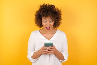 Güzel, çekici, şaşırmış bir kadının portresi cep telefonuyla boş zamanlarında sohbet ediyor. 
