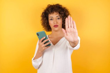 Akıllı telefonuyla mesajlaşan kadının portresi açık elle dur işareti yaparken ciddi ve kendinden emin bir ifadeyle savunma jesti yapıyor.