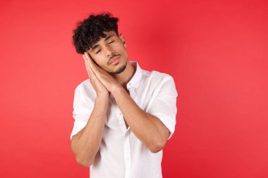 Kıvırcık saçlı, elleri birbirine poz veren ve gözleri kapalı gülümseyen genç yakışıklı bir adam..