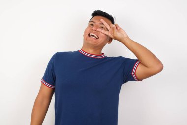 Yakışıklı genç adam barış sembolü yapıyor. Yüzünde parmaklar, gülümseyerek zaferi gösteriyor.