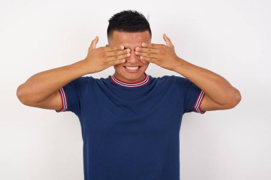 Genç yakışıklı adam elleri ile gözlerini kapayarak neşeli ve komik gülümsüyor. Kör kavram.