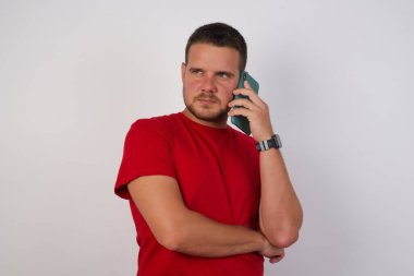 Üzgün, esmer, beyaz, kırmızı tişörtlü adam akıllı telefondan konuşuyor. 