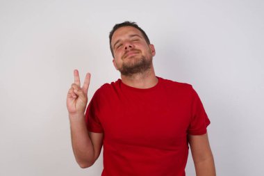 Gözleri kapalı gülümseyen, gülümseyen, kameraya göz kırpan bir adam zafer işareti yapıyor. İki numara..