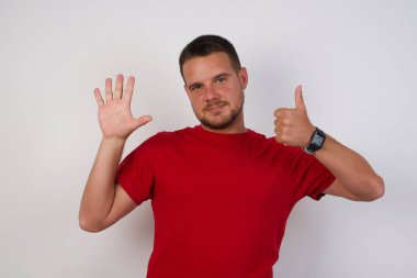 Kırmızı tişörtlü adam altı numarayı gösterip işaret ederken kendinden emin ve mutlu gülümsüyor.