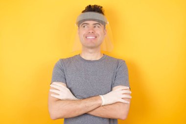 Plastik şapkalı adam kollarını kavuşturuyor, güzel görünüyor, gülümsüyor.