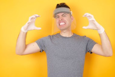 Plastik şapkalı bir adam sarı arka planda poz veriyor öfkeden çıldırmış bir şekilde bağırıyor, elleri boğmaya çalışıyor, deli gibi bağırıyor..