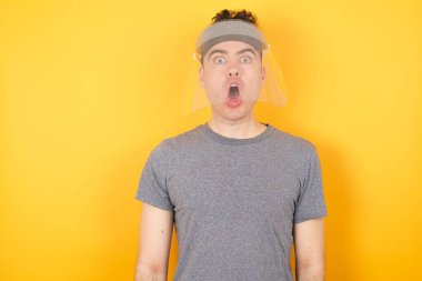 - Aman Tanrım! Tişört ve yüz maskesi takmış genç beyaz bir adam tecrit edilmiş sarı arka planda dikilip kameraya şok olmuş bir ifadeyle bakıyor. Beklenmedik bir şekilde bağırıyor., 