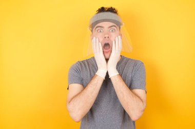 Ürkmüş, korkmuş, beyaz tişört giyen, sarı arka planda duran, dükkandaki fiyatlarla şoka uğramış, bir şeyler alacak parası olmayan, insan ve insan duyguları kavramı olan genç beyaz bir adamın stüdyo fotoğrafı.