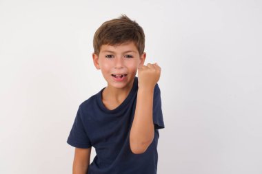 Güzel bir çocuk, izole edilmiş beyaz arka planda dikilen sıradan bir tişört giyer kızgın ve öfkeli bir şekilde yumruğunu kaldırır ve öfkeyle bağırır. Öfke ve agresif kavram.