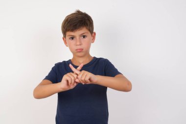 Güzel çocuk, izole edilmiş beyaz arka planda sarı duvarın önünde duran sıradan bir tişört giyiyor. Reddedilme ifadesi negatif işaret yaparak parmaklarını çapraz yapıyor mu?.