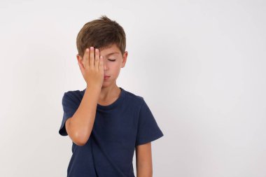 İzole edilmiş beyaz arka plan üzerinde günlük tişört giyen güzel çocuk, esnemekten yorgun düşmüş, yarı yüz, göz ve ağız ellerle kapatıyor. Yüzüm acıyor..