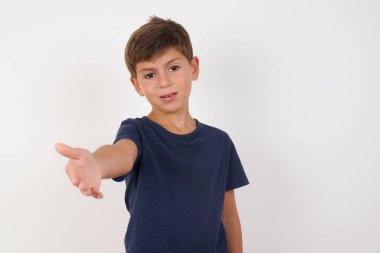 Güzel bir çocuk, izole edilmiş beyaz arka plan üzerinde sıradan bir tişört giyip selamlaşma ve dostça bir şekilde el sıkışırken gülümsüyor. Başarılı bir iş..