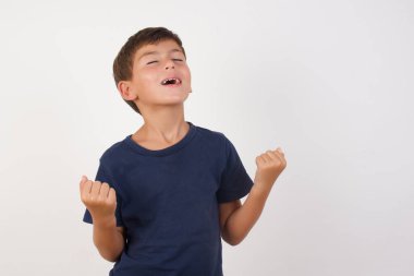 Güzel çocuk, izole edilmiş beyaz arka plan üzerinde sıradan bir tişört giyip kolları açık ve gözleri kapalı bir şekilde başarının şaşkınlığını ve şaşkınlığını kutluyor. Kazanan konsept.