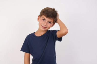 Güzel bir çocuk, izole edilmiş beyaz arka plan üzerinde sıradan bir tişört giyiyor, kafası karışmış ve bir şeyi merak ediyor. Elini başının üstünde tutuyor, şüpheyle emin değil. Düşünceli kavram.