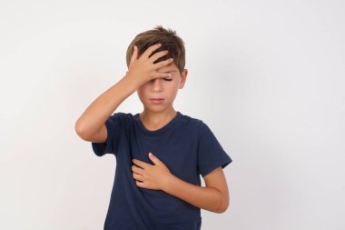 İzole edilmiş beyaz arka plan üzerinde duran sıradan tişört giyen güzel çocuk hastalık, ateş, grip ve soğuk algınlığı için alnına dokunuyor..