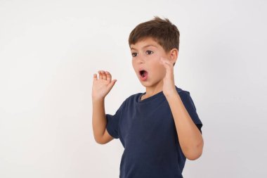 Güzel çocuk günlük tişört giyip izole edilmiş beyaz arka planda dikiliyor, yüksek sesle bağırıyor, gözleri açık ve elleri gergin tutuyor..
