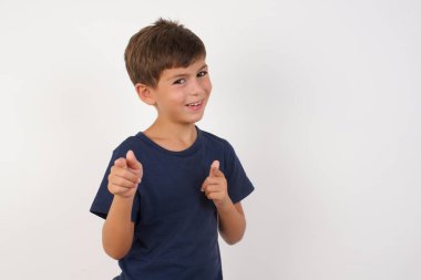 Güzel çocuk, izole edilmiş beyaz arka plan üzerinde sıradan bir tişört giyip mutlu ve komik yüzüyle kamerayı işaret ediyor. İyi enerji ve titreşimler. 