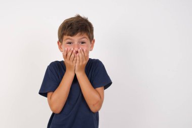 Neşeli, rahat bir tişört giyen, beyaz arka planda duran, neşeyle kıkırdayan, ağzı kapatan, tek başına eğlenen, doğal kahkahalar atan, pozitif hikayeler duyan, ya da komik anekdotlar dinleyen güzel çocuk.