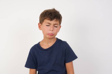 Kasvetli, kasvetli, sıradan tişörtlü güzel bir çocuğun izole edilmiş beyaz arka plan üzerinde durması, sorunları ve zorlukları var, alt dudak kıvrımları ve umutsuzluk içinde gözlerini kapatması, umutsuzca çabalar sonrasında depresyonda olması. 