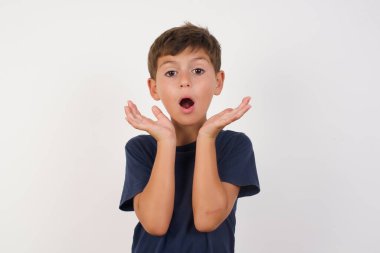 Şaşırmış, korkmuş, sıradan tişörtlü güzel bir çocuk izole edilmiş beyaz arka plan üzerinde duruyor, belirsizlikle jestler yapıyor, kameraya bakıyor, şaşırmış bir şekilde hileli soruya cevap vermiyor, insanlar, vücut dili, duygu kavramı.