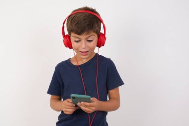 İzole edilmiş beyaz arka planda duran günlük tişört giyen mutlu, güzel çocuk akıllı telefon ekranına odaklanırken kendini iyi hissediyor. İnsanlar, teknoloji, yaşam tarzı