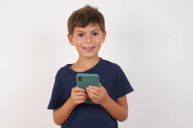 Fotokopi uzay fotoğrafı. Güzel bir çocuğun günlük tişörtler giyip izole edilmiş beyaz arka planda dururken elinde telefon tutarken çekilmiş.