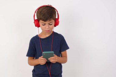 İzole edilmiş beyaz arka planda dikilen sıradan tişörtler giyen güzel bir çocuğun portresi, cep telefonu kullanması sosyal medyada inanılmaz haberler okuyor, bağırıyor, vay canına, şık kıyafetler giyiyor.