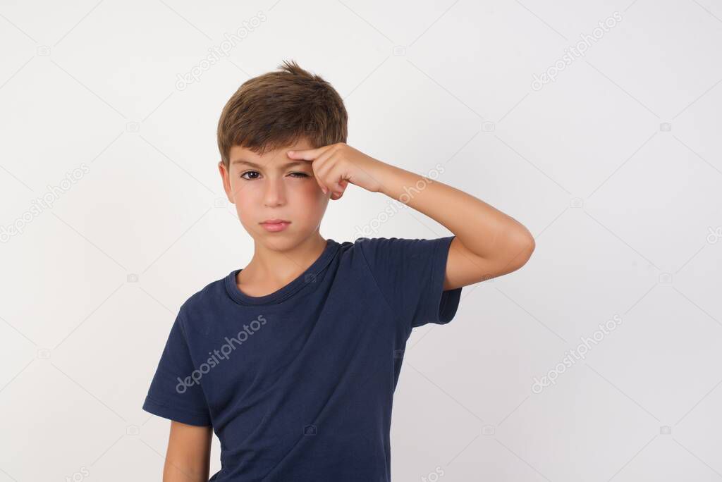 Beautiful kid boy wearing casual t-shirt standing over isolated white background, pointing unhappy at pimple on forehead, blackhead  infection. Skincare concept.
