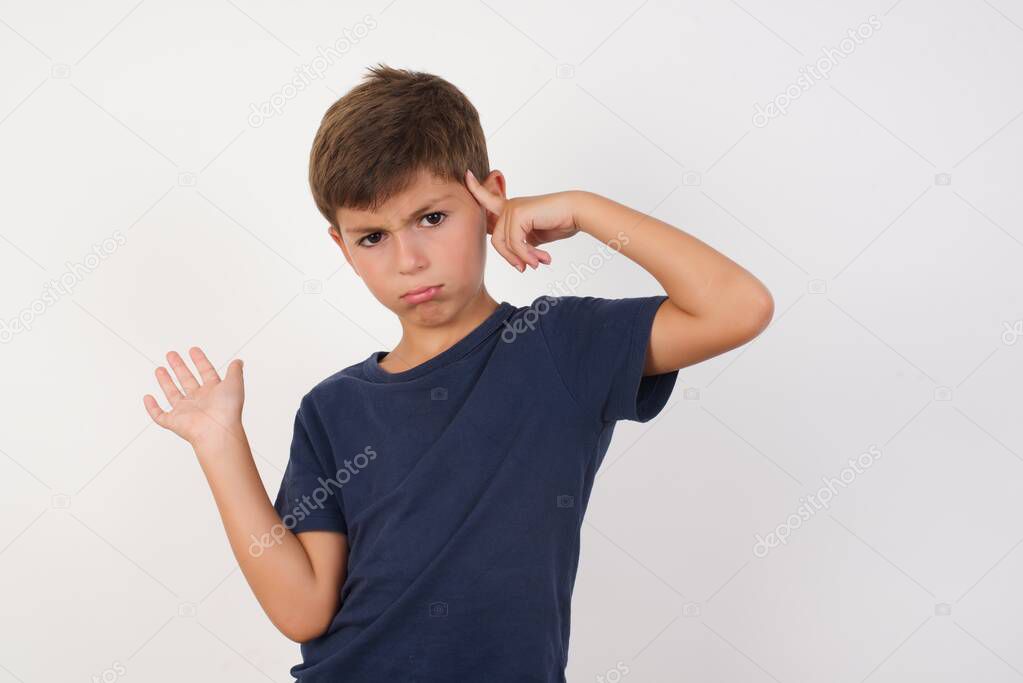 Beautiful kid boy wearing casual t-shirt standing over isolated white background, confused and annoyed with open palm showing copy space and pointing finger to forehead. Think about it.