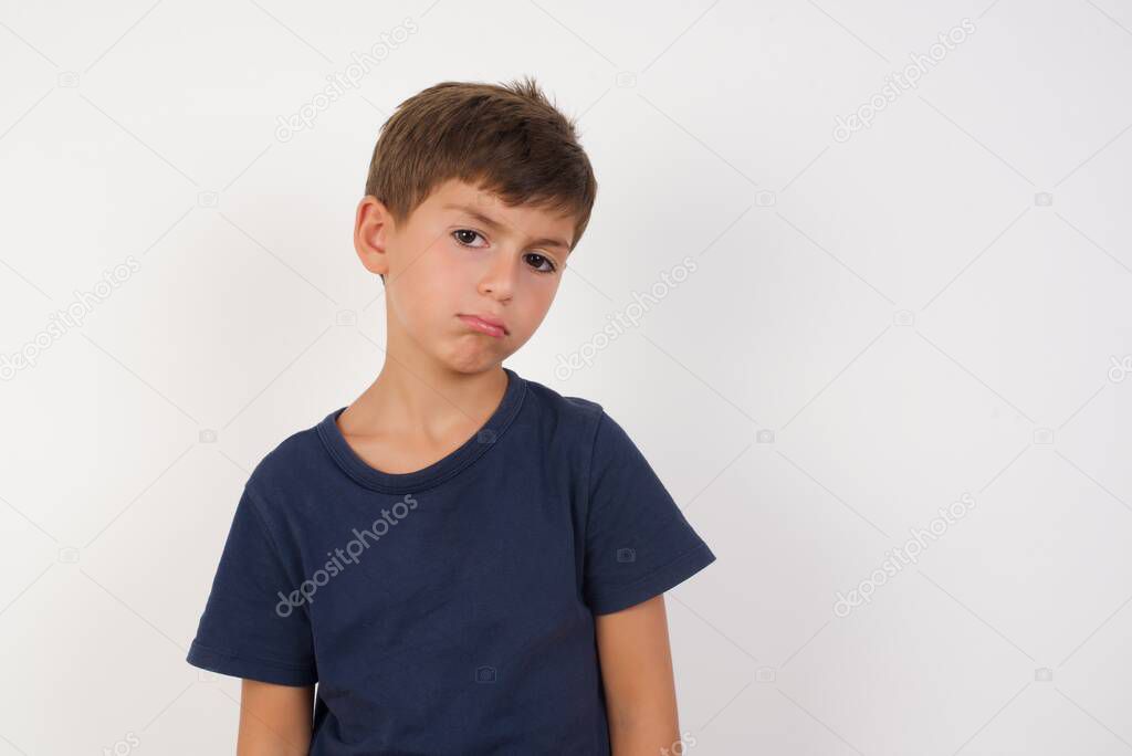 Portrait of displeased upset  Beautiful kid boy wearing casual t-shirt standing over isolated white background, frowns face as going to cry, being discontent and unhappy as can't achieve goals,  Disappointed young man has troubles