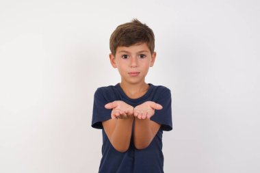 Güzel bir çocuk günlük tişört giyip izole edilmiş beyaz arka planda duruyor. Elinde avuç içi açık bir şey tutuyor ve kameraya sunuyor..