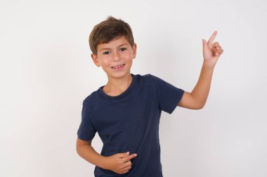 İzole edilmiş beyaz arka planda duran günlük tişört giyen güzel çocuk parmak boş uzay satış müdürünü işaret ediyor.