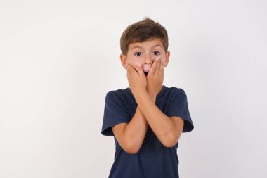 Güzel çocuk, izole edilmiş beyaz arka plan üzerinde sıradan bir tişört giyiyordu. Ağzını yanlışlıkla ellerle kapatıyordu. Gizli konsept.