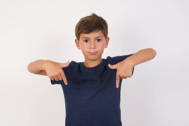 Güzel çocuk, izole edilmiş beyaz arka plan üzerinde iki parmağıyla fotokopi alanını gösteren sıradan bir tişört giyiyor. Reklam için yer