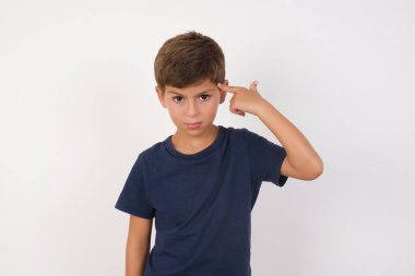 Mutsuz, sıradan tişörtler giyen, beyaz arka planda duran, dudaklarını kıvıran, intihar hareketi yapan, her şeyden bıkmış, el ile şakağına ateş eden güzel çocuk., 