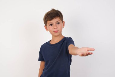 Güzel çocuk, günlük tişört giyip izole edilmiş beyaz arka planda dikiliyor, gülümsüyor, avuç içi kadar yardım ve kabullenme teklif ediyor..