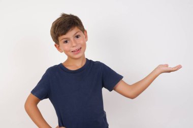 Güzel çocuk, izole edilmiş beyaz arka planda duran sıradan bir tişört giyiyor, mutlu ve neşeli hissediyor, sana gülümsüyor ve hoş geldin diyor, seni dostça bir jestle içeri davet ediyor. 