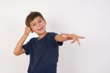 Güzel çocuk, izole edilmiş beyaz arka plan üzerinde duran, neşeli bir şekilde gülümseyen ve kameraya doğru bakan sıradan bir tişört giyer. Daha sonra seni arar, telefonla konuşur. 