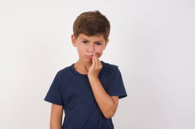 Güzel bir çocuk, izole edilmiş beyaz arka planda dikilen sıradan bir tişört giyiyor diş ağrısı ya da diş hastalığından dolayı ağıza acı dolu bir ifadeyle dokunuyor..