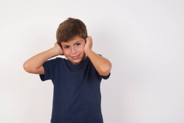 Güzel bir çocuk, izole edilmiş beyaz arka planda dikilen günlük tişört giyiyor, yüksek sesli müzik sesi için kulakları parmaklarıyla parmaklarıyla kapatıyor. Sağır kavramı.