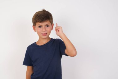 Güzel çocuk, izole edilmiş beyaz arka planda duran sıradan bir tişört giyiyordu. Bir numaralı parmağını gösteriyordu ve gülümsüyordu. Kendinden emin ve mutluydu..