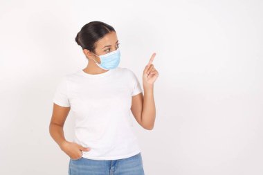 Tıbbi maske takan gülümseyen Arap kadın izole edilmiş beyaz arka planda dikilip kameraya bakıyor. 