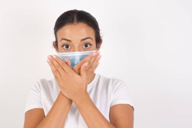 İzole edilmiş beyaz arka planda duran tıbbi maske takan genç bir Arap kadın yanlışlıkla ağızlarını kapatarak şok geçirdi. Gizli konsept.