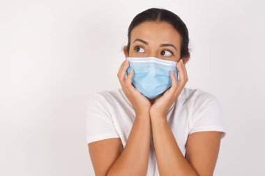 Tıbbi maske takan genç bir Arap kadının tecrit edilmiş beyaz arka planının başında dikilip kopyalanmış uzaya bakması ve gelecekteki olaylar hakkında düşünceleri olması ilham verici. 