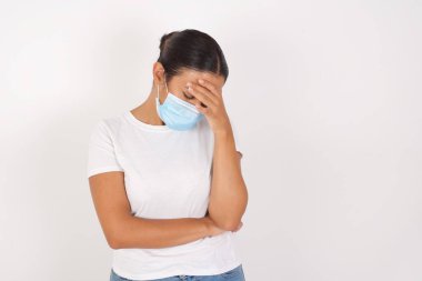 Çok üzgün ve yalnız, tıbbi maske takan genç bir Arap kadın izole edilmiş beyaz arka planda duruyor. Ağlıyor, 