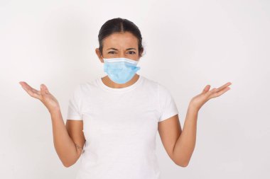 Tıbbi maske takan öfkeli genç Arap kadın şaşkınlık içinde beyaz arka plan jestlerinin başında duruyor, hoşnutsuzlukla yüzünü ekşitiyor, akşam yemeği hazırlamak için ürün almayı unuttuğunu söylüyor. Olumsuz duygular ve yüz ifadesi