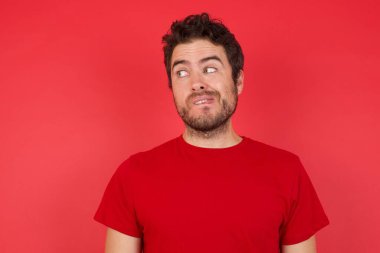 Stüdyoda kırmızı gömlek giyen, dudağını ısıran ve boş uzaya bakan beyaz bir adam.