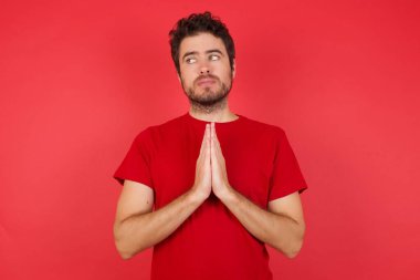 Genç bir adam, kırmızı arka planda el ele tutuşup bir fikir oluşturma planına karşı çıkıyor. Bak askance. 