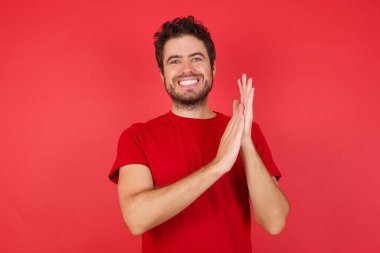 İyimser mutlu adam kırmızı stüdyoda heyecanlı, kazanan elleriyle alkışlıyor. 