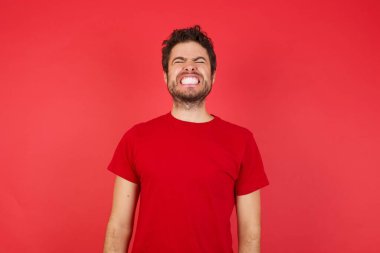 Kırmızı arka planda gözleri kapalı dişlerini gösteren yakışıklı beyaz bir adam. 